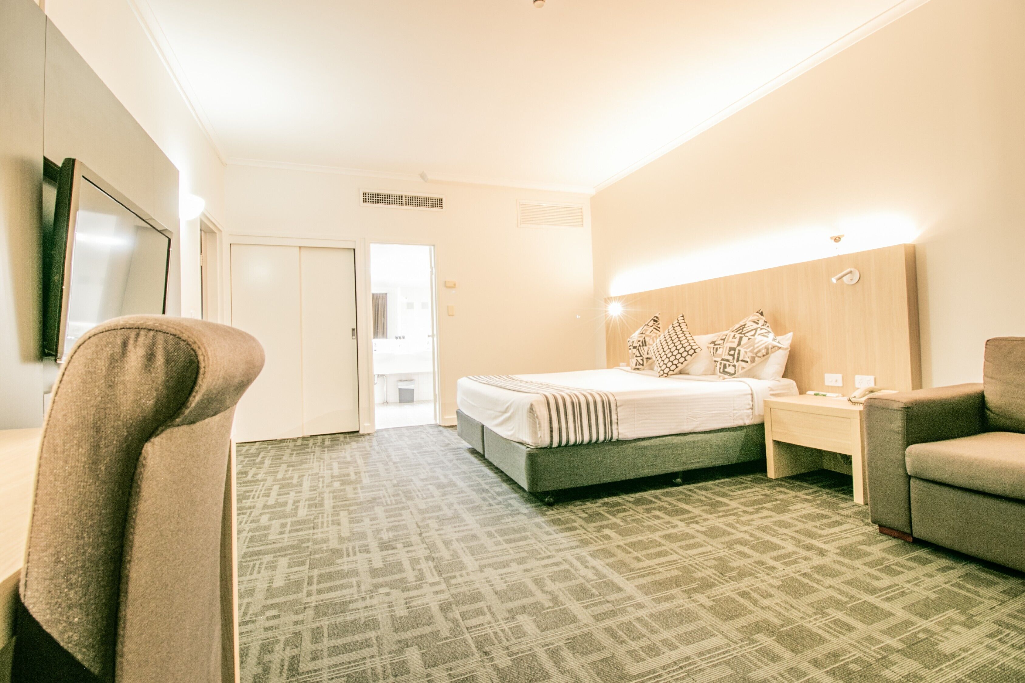A hotel room with a bed, a chair, a nightstand, and a TV.