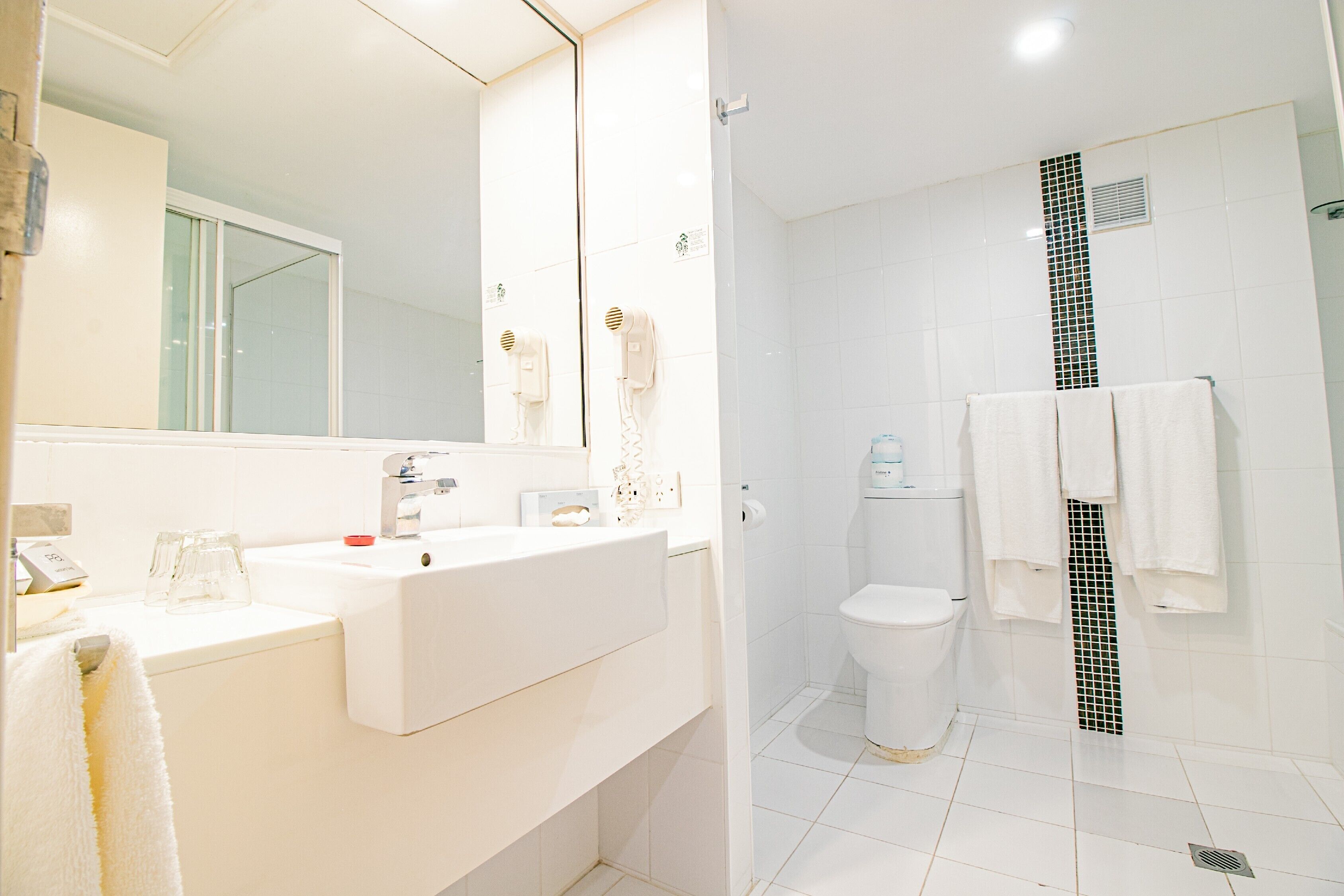 A bathroom with a white sink, mirror, and toilet. There are towels hanging on the wall and a shower curtain.
