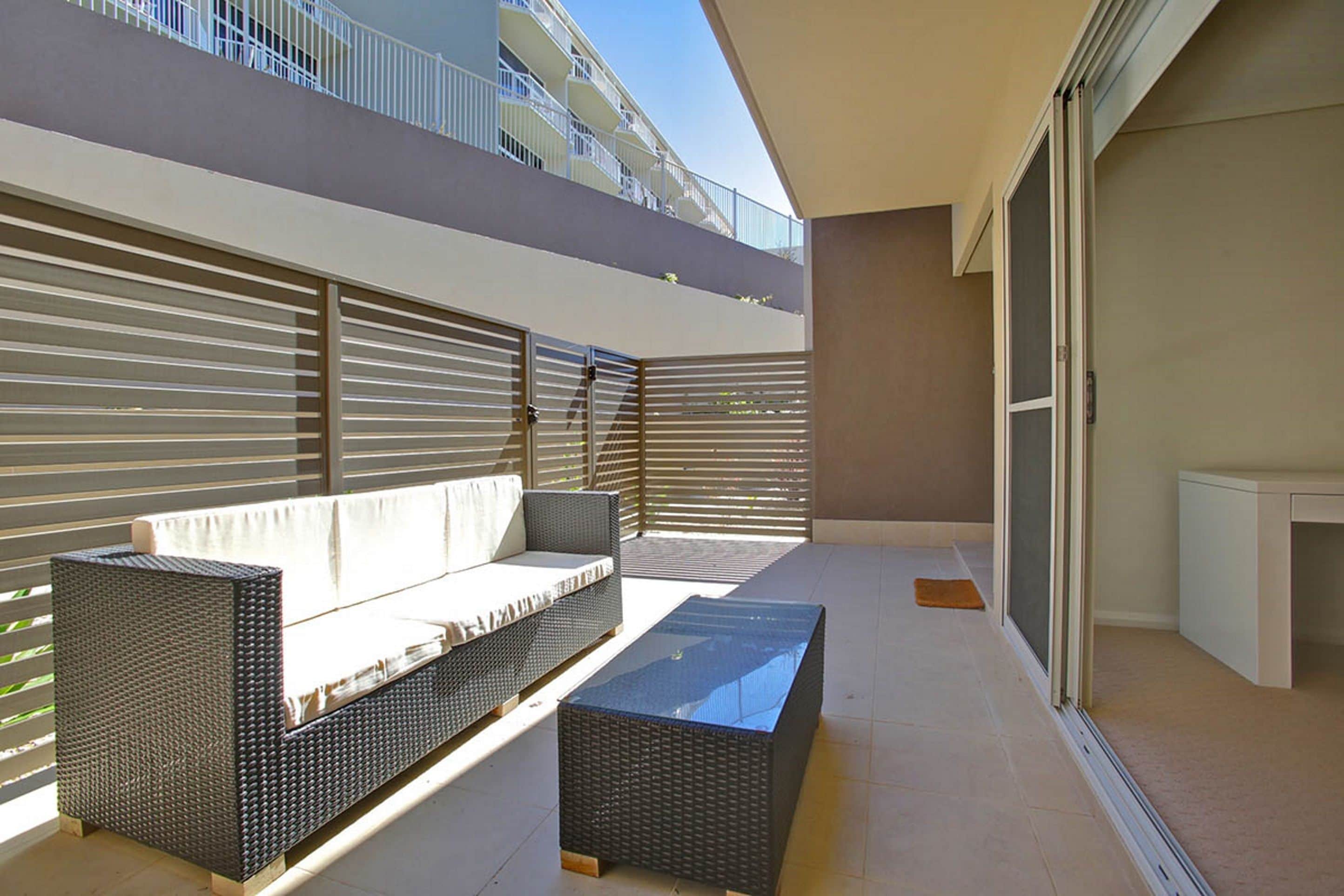 A balcony with a wicker sofa, a small table, and a sliding glass door.