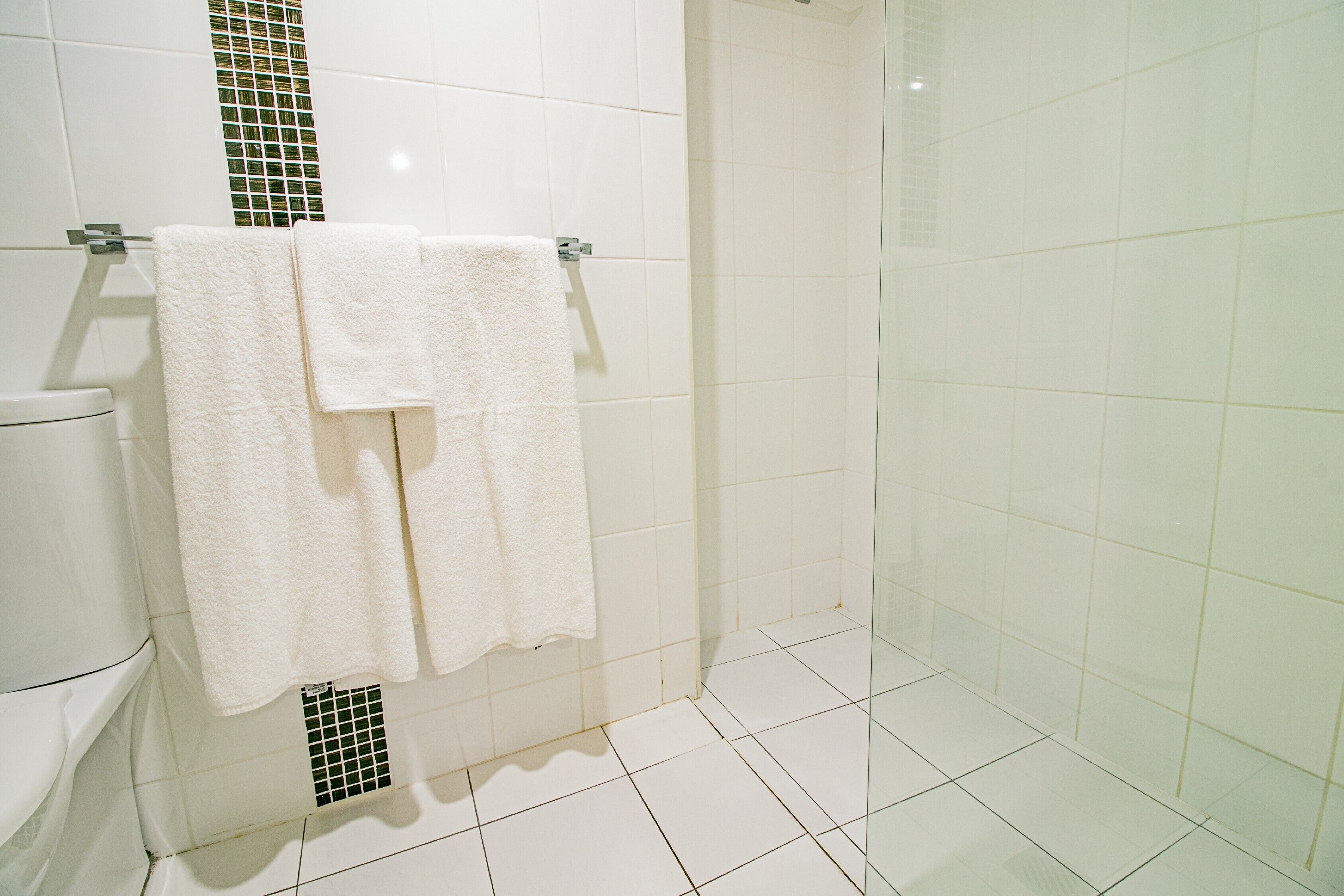 A bathroom with white tiles, a glass shower enclosure, and two white towels hanging on a metal towel rack.