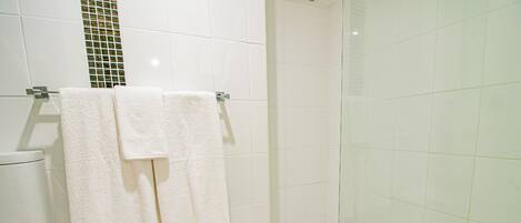 A bathroom with white tiles, a glass shower enclosure, and two white towels hanging on a metal towel rack.