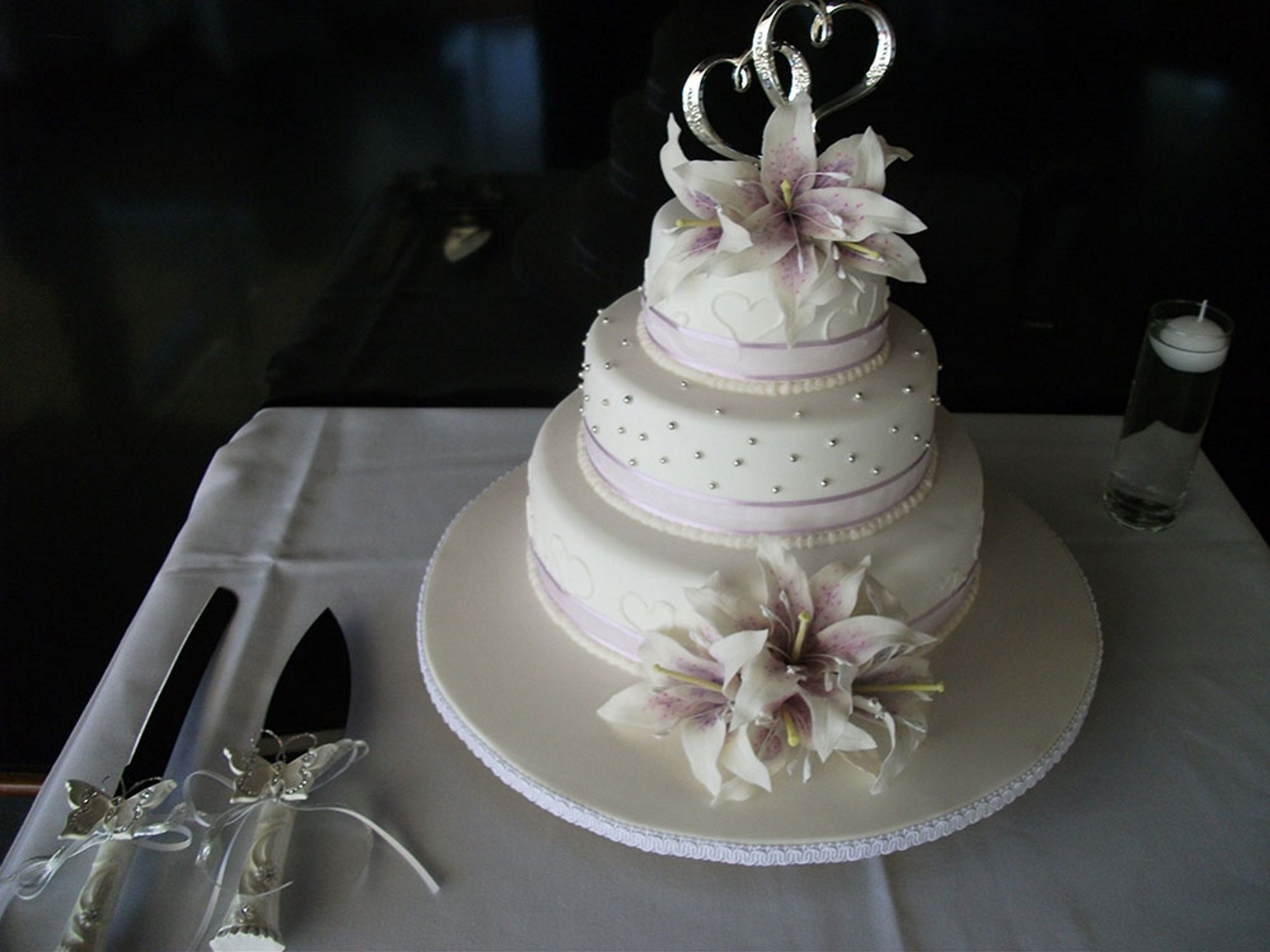 Un gâteau de mariage à trois étages, décoré de blanc et de violet, posé sur une nappe blanche.