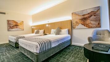 A hotel room with two beds, a wooden headboard, a green carpet, and two abstract paintings on the walls.