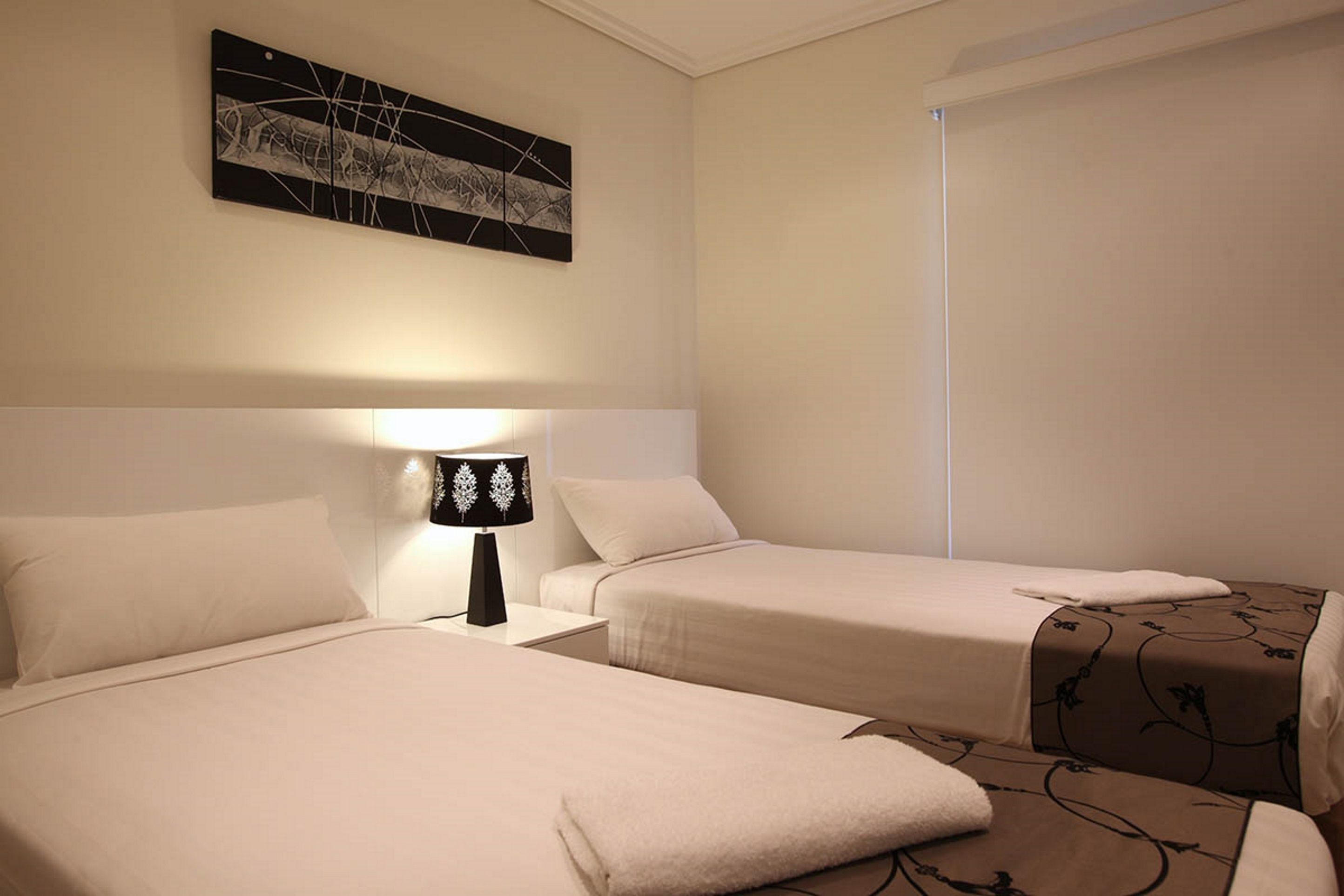 A hotel room with two beds, a nightstand with a lamp, and a wall-mounted artwork.