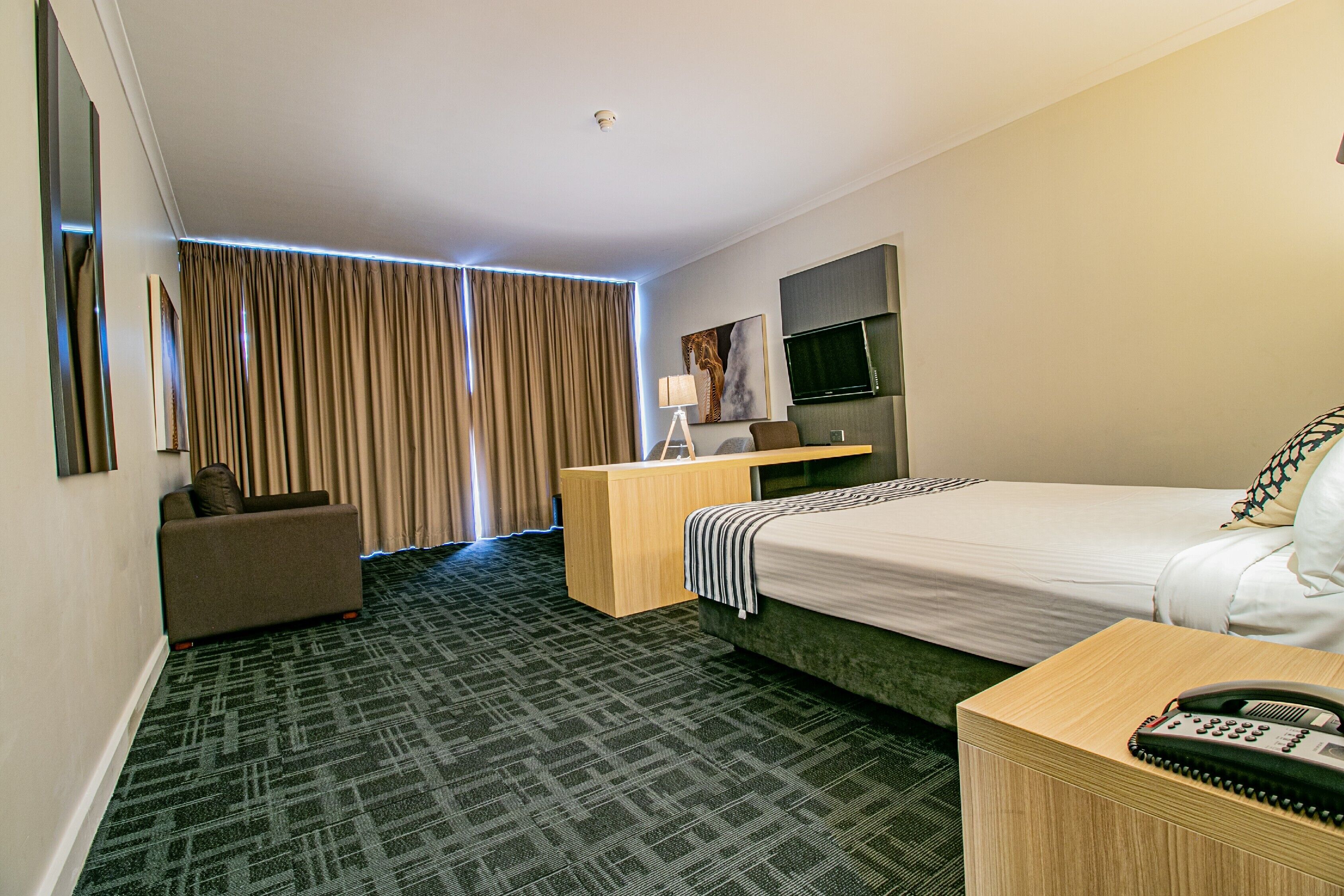 A hotel room with a bed, a desk, a chair, a TV, and a window with curtains.
