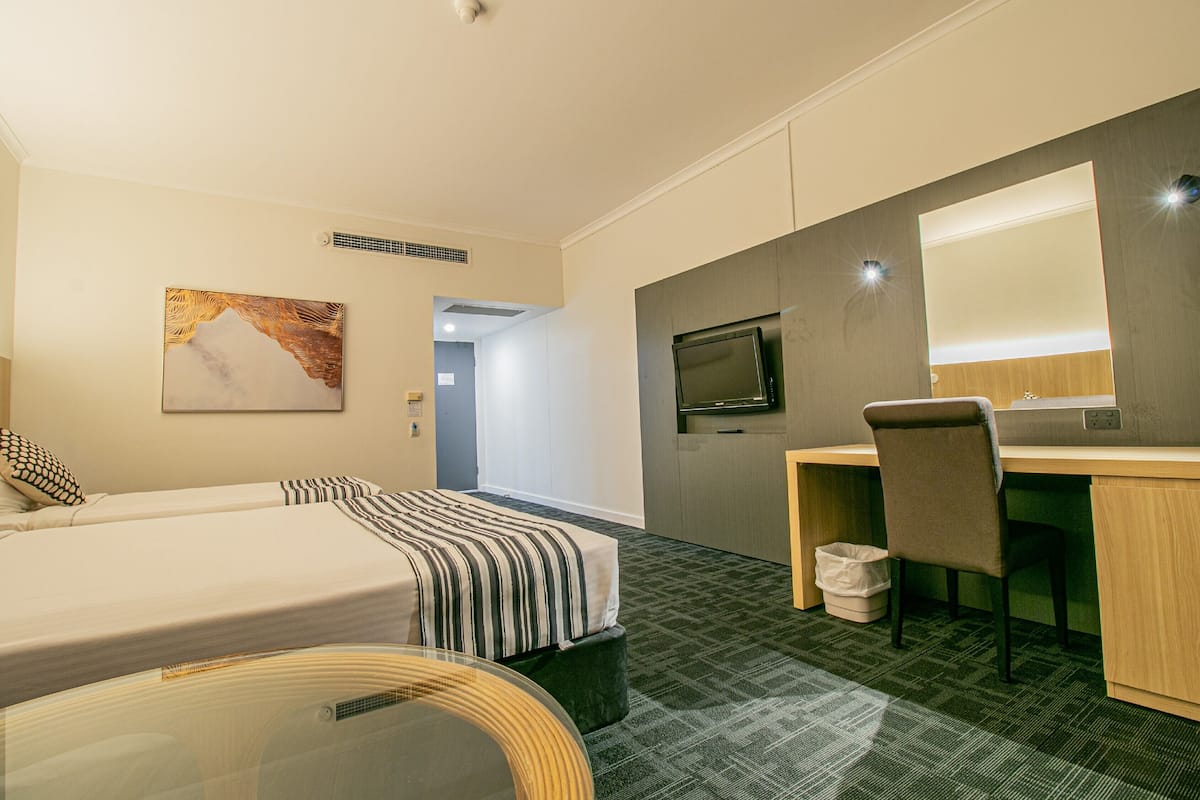 A hotel room with a bed, a desk, a chair, a television, and a painting on the wall.