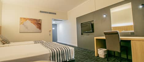 Habitación de hotel con cama, escritorio, silla, televisor y un cuadro en la pared.