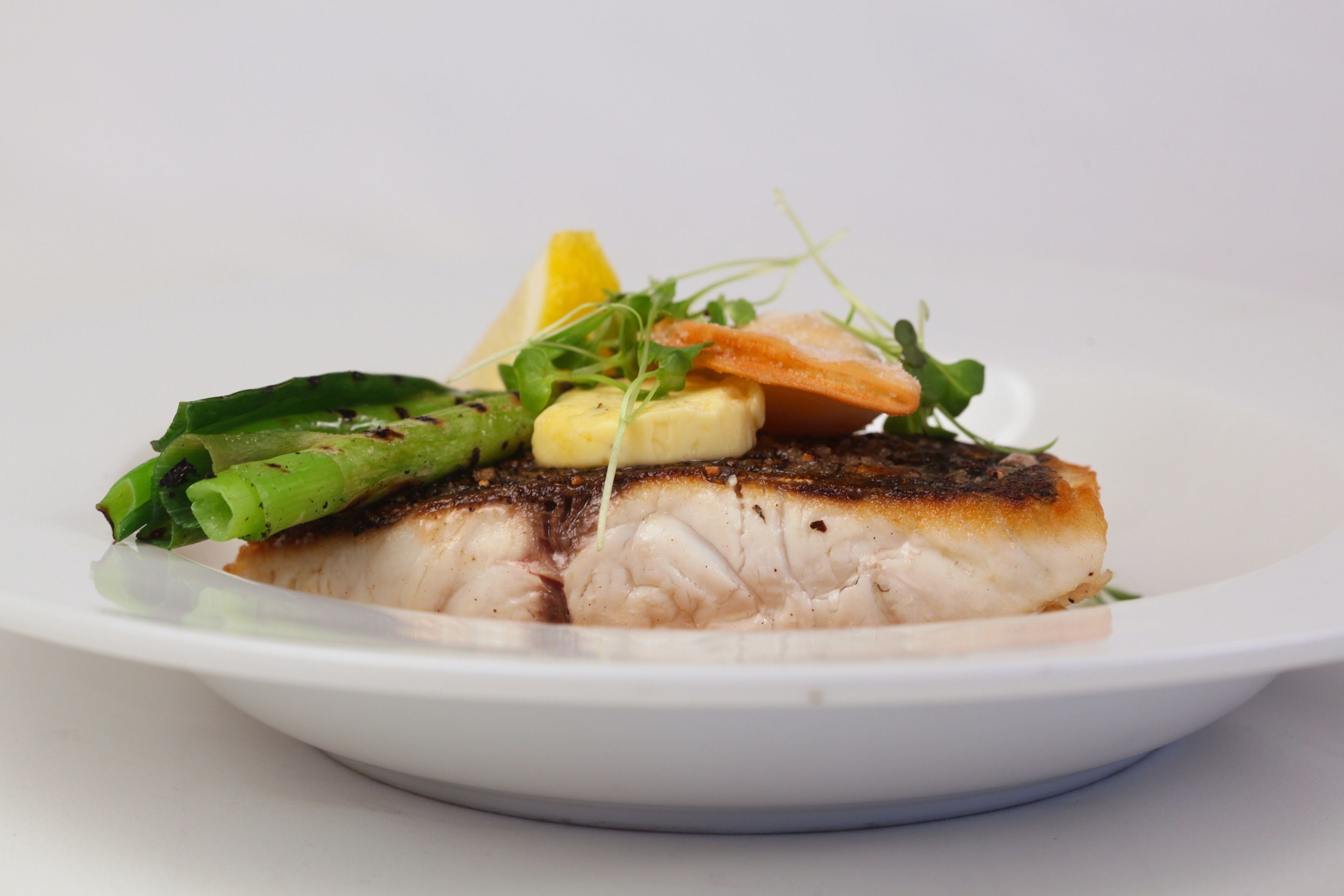 A plate of food with a piece of grilled fish, green vegetables, and a lemon wedge.