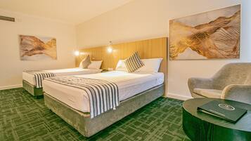 A hotel room with two beds, a green carpet, a wooden headboard, a gray armchair, and a round table with a laptop.