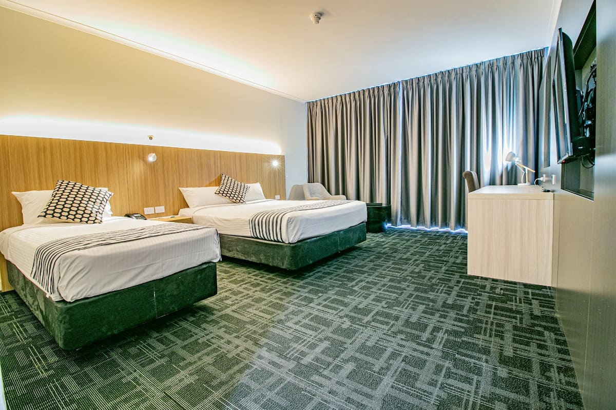 A hotel room with two beds, a desk, a chair, a TV, and a large window with curtains.