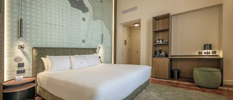 A neatly arranged hotel room with a large bed, a small side table, a green ottoman, a wooden cabinet, and a map on the wall.