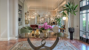 A spacious living area with a glass-top coffee table, a large mirror, and a chandelier.