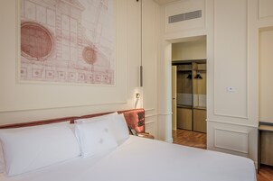 Una camera d'albergo con un letto grande, un comodino, una lampada fissata al muro e un ingresso che dà su un bagno.