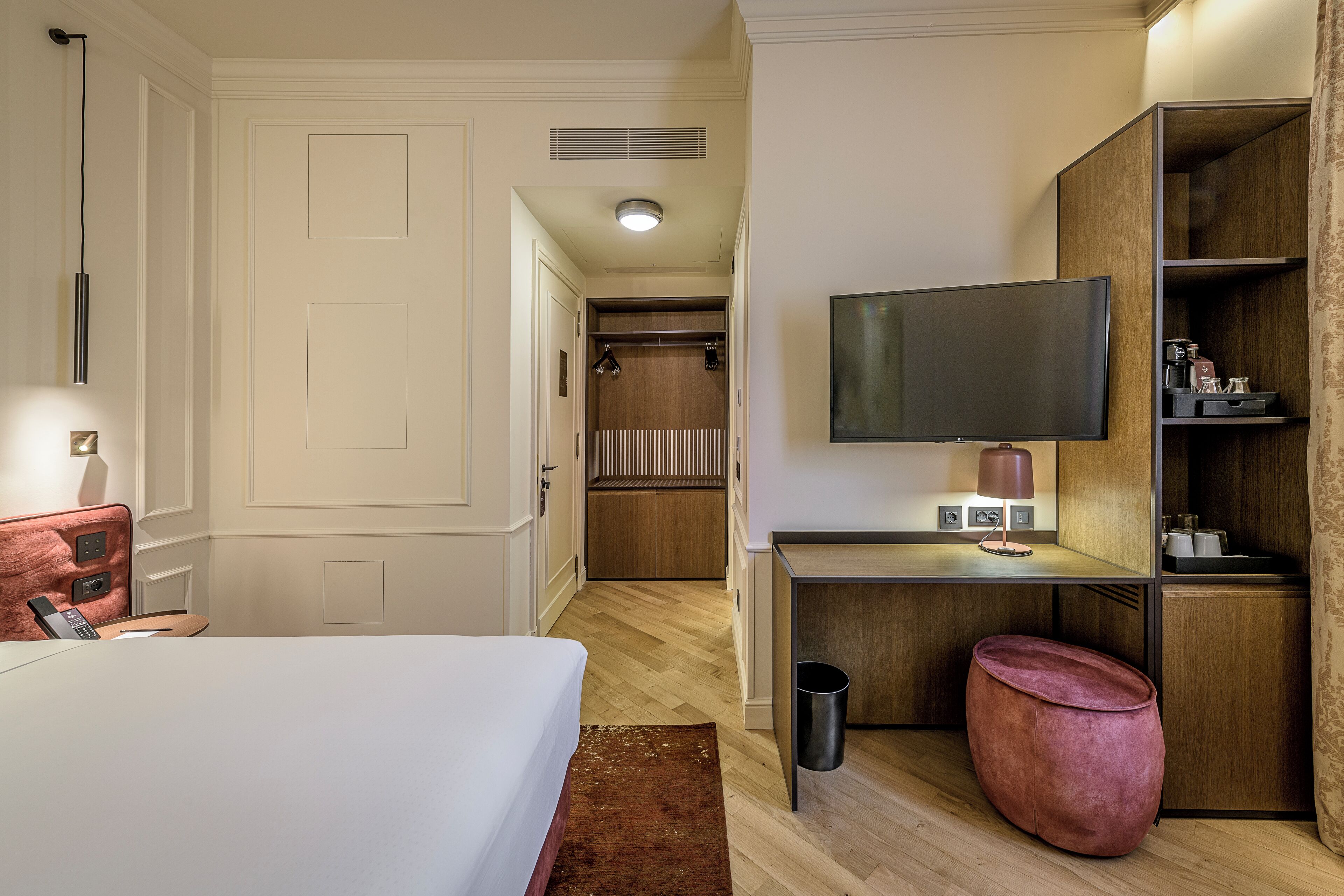 Una camera d'albergo con un letto, una scrivania con televisore, un armadio e un piccolo angolo salotto.
