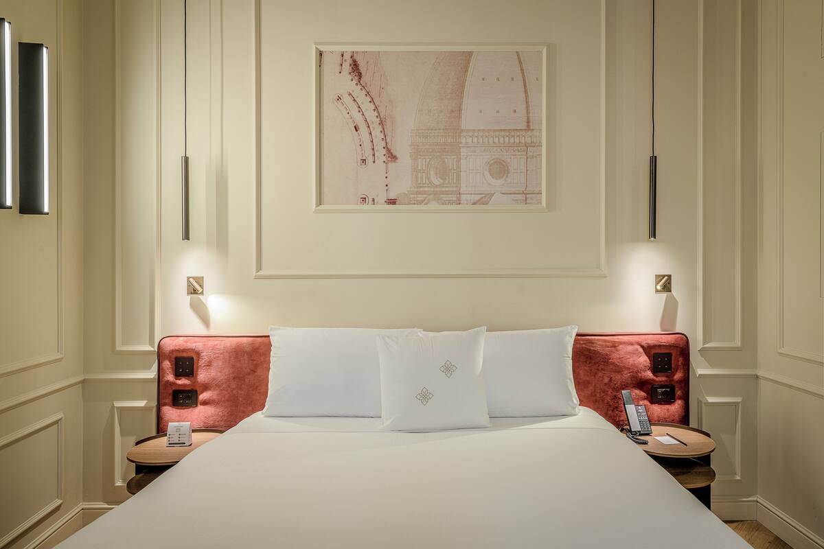 A hotel room with a large bed, two bedside tables, a telephone, and a framed picture on the wall.