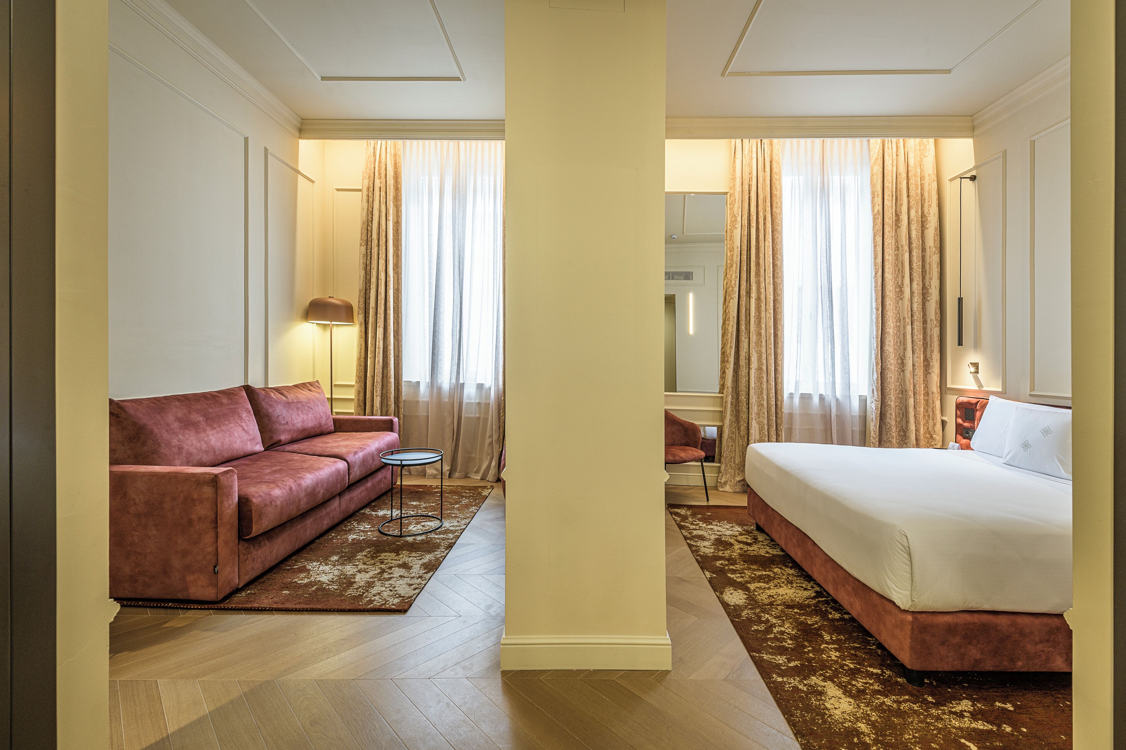 A hotel room with a bed, a sofa, a small table, and a lamp.