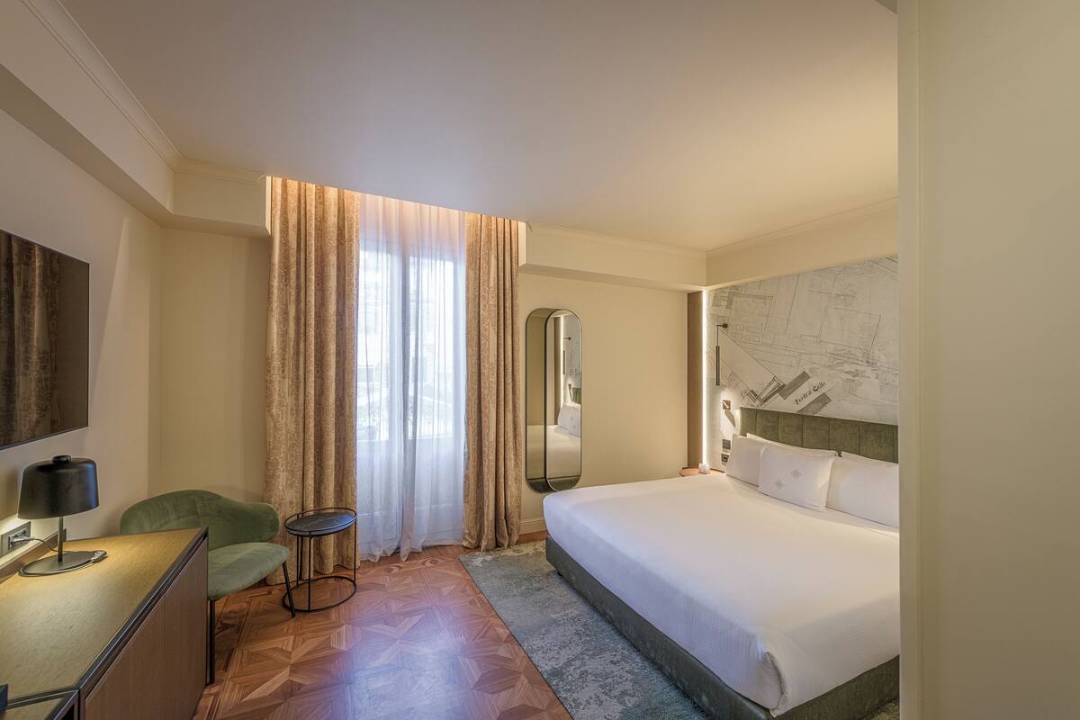 A hotel room with a bed, a desk, a chair, a mirror, and a map on the wall.