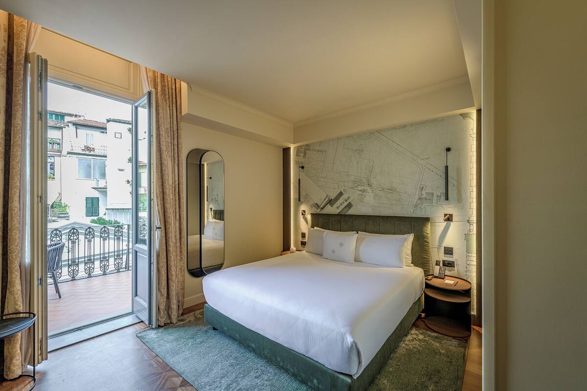 A hotel room with a large bed, a nightstand, a mirror, and a view of the outside balcony.