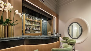 A bar area with a marble countertop, green bar stools, and a wooden panel backdrop.