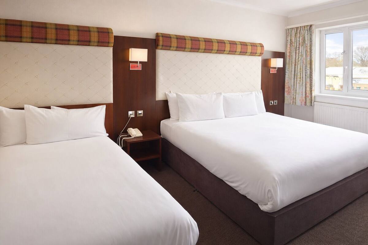A hotel room with two beds, a nightstand with a telephone, and a window with curtains.