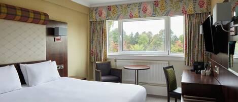 A hotel room with a bed, a desk, a chair, a television, and a window with curtains.