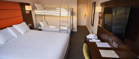 Habitación de hotel con una cama grande, un escritorio con silla, un televisor y una literas.