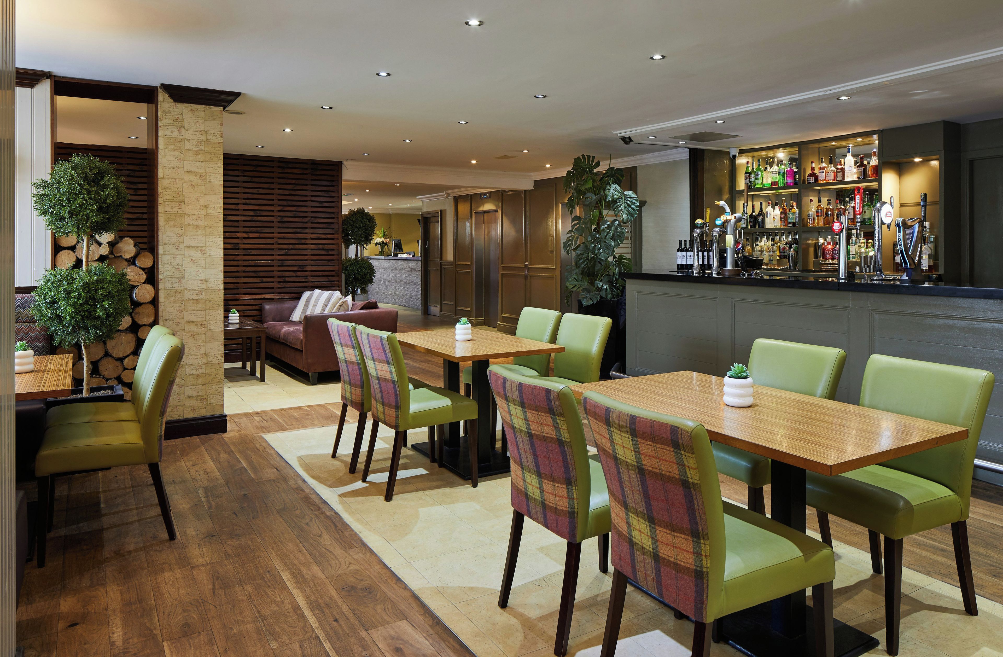 Un ristorante con tavoli e sedie in legno, un'area bar con bottiglie e un banco reception.