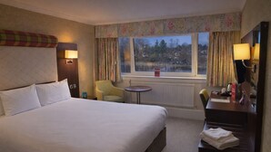 Een hotelkamer met een groot bed, een bureau, een stoel, een tafeltje en een raam met gordijnen.