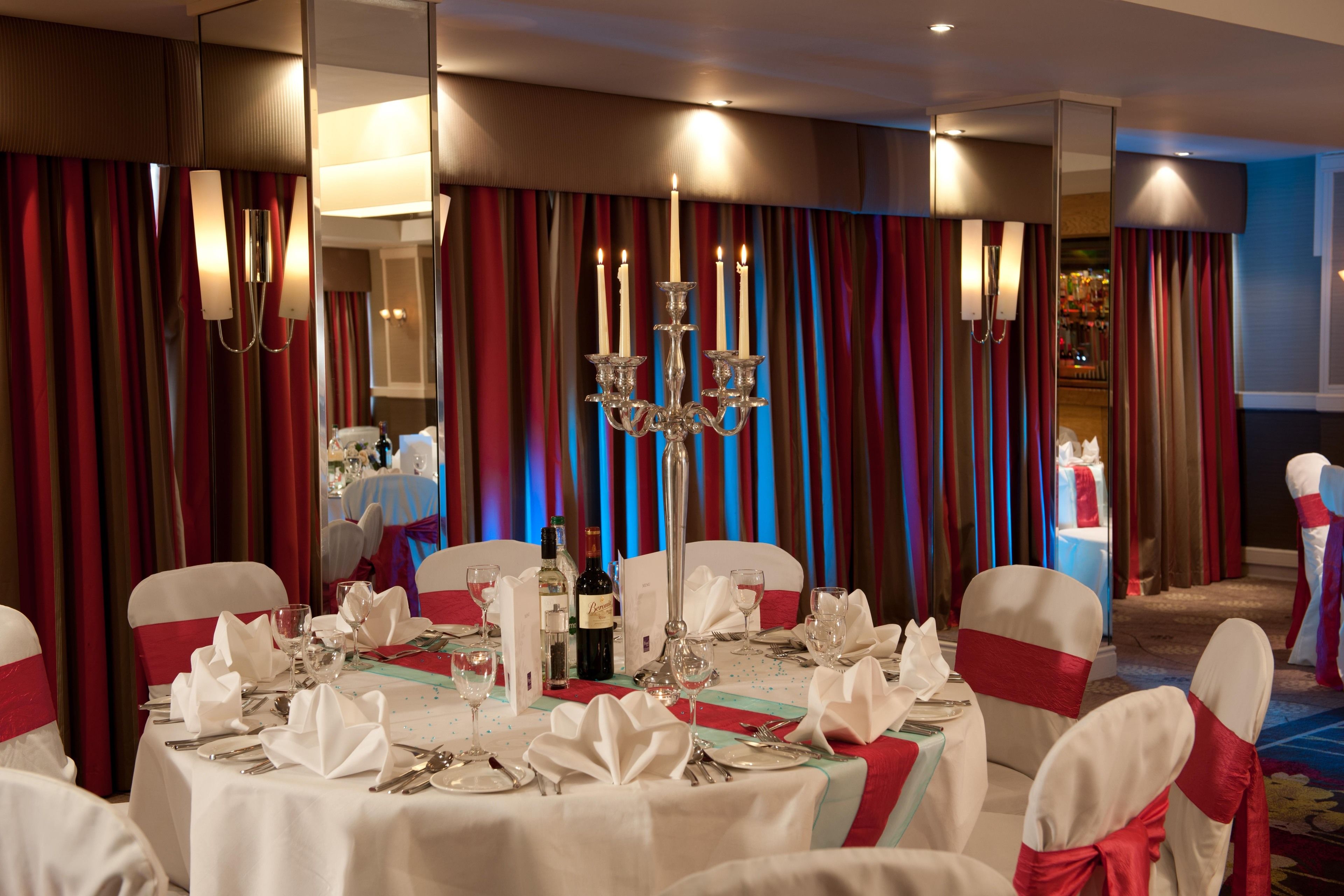 A banquet hall with round tables set for a formal event, featuring white tablecloths, silverware, and candles.
