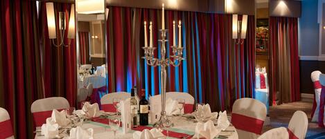 A banquet hall with round tables set for a formal event, featuring white tablecloths, silverware, and candles.