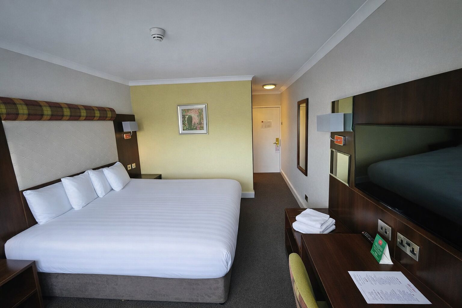 Une chambre d’hôtel avec un grand lit, un bureau avec une chaise, une télévision et une porte donnant sur une autre pièce.