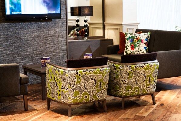 A living room with a sofa, two patterned ottomans, a coffee table, and a flat-screen TV mounted on the wall. - Leonardo Inn Glasgow West End (Glasgow)