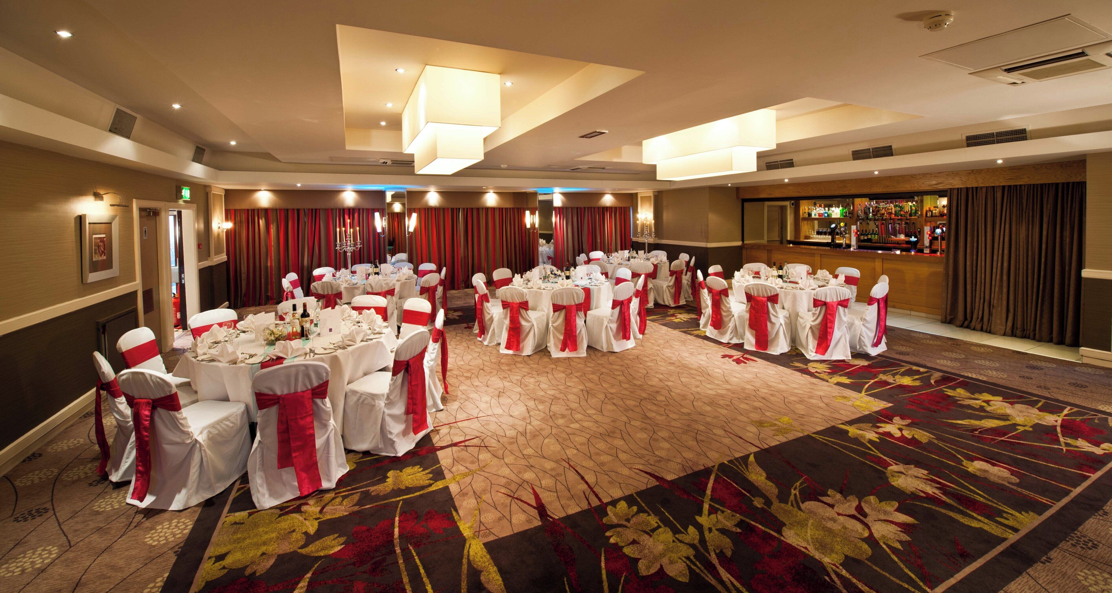 A banquet hall with round tables set for a formal event, featuring white tablecloths and red sashes.