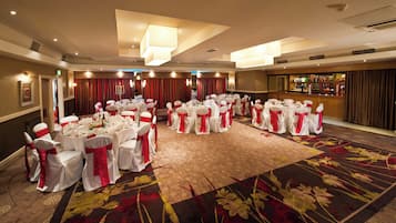 A banquet hall with round tables set for a formal event, featuring white tablecloths and red sashes.