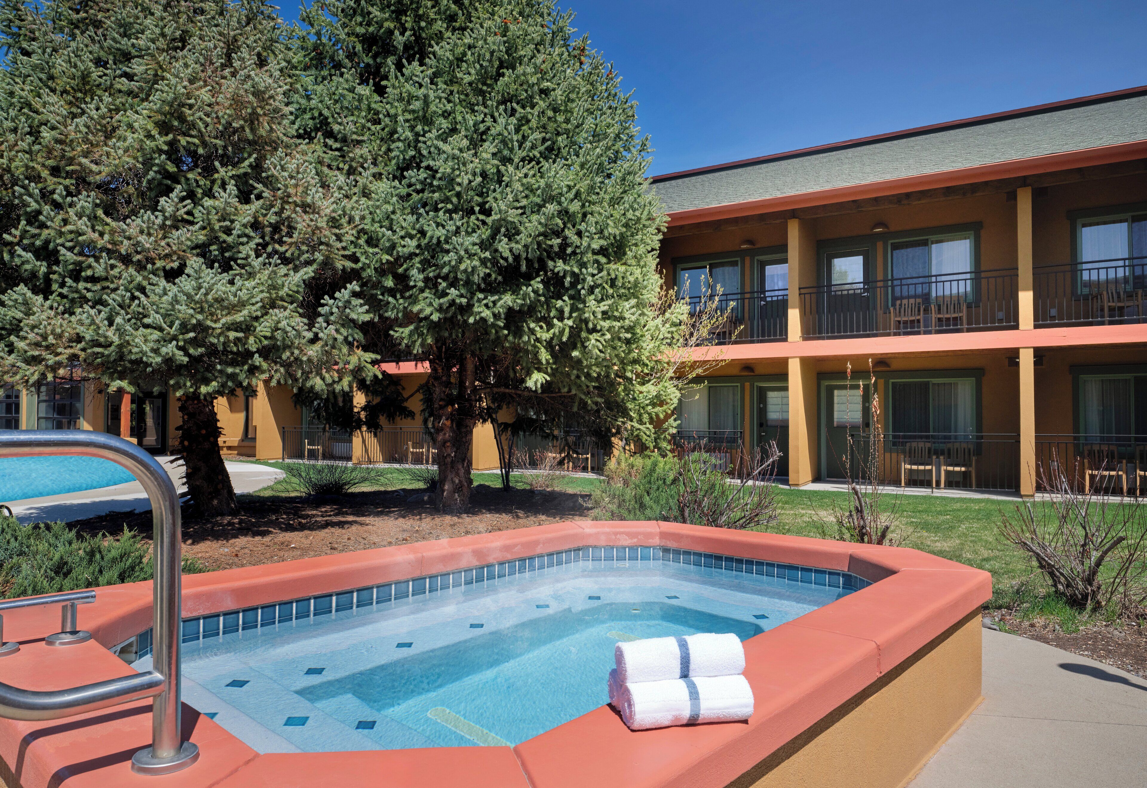 A swimming pool with a red border, a tree, and a building with balconies in the background.