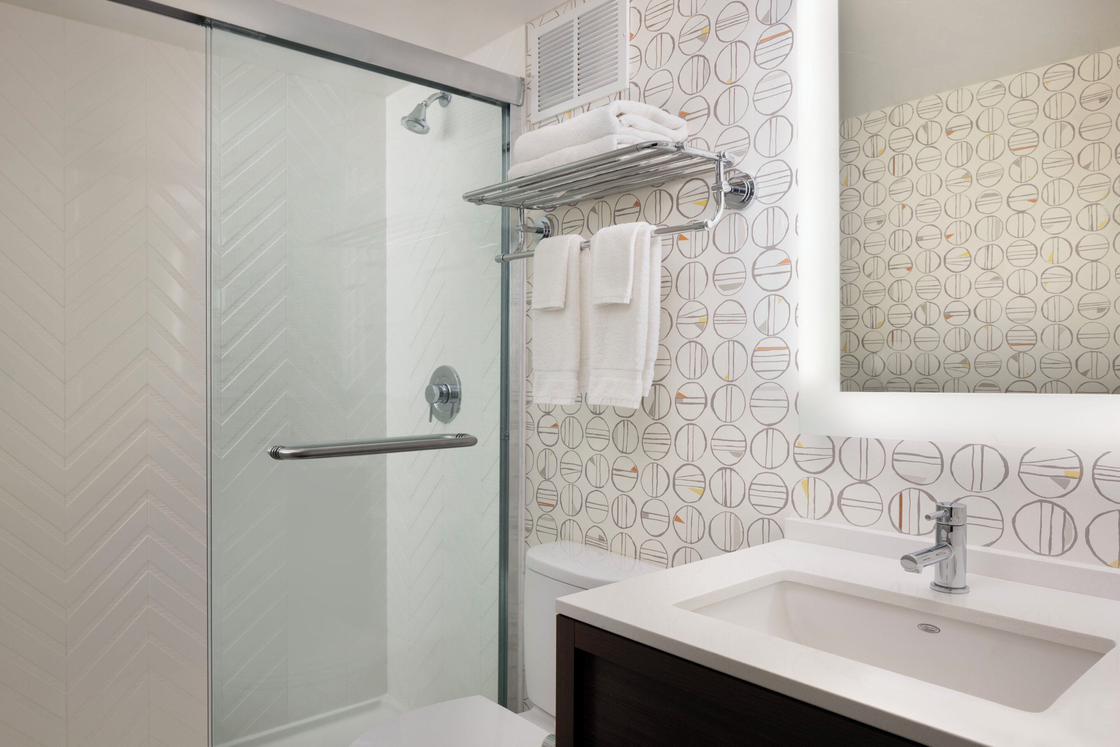 A modern bathroom with a glass shower door, a white sink, and a towel rack.