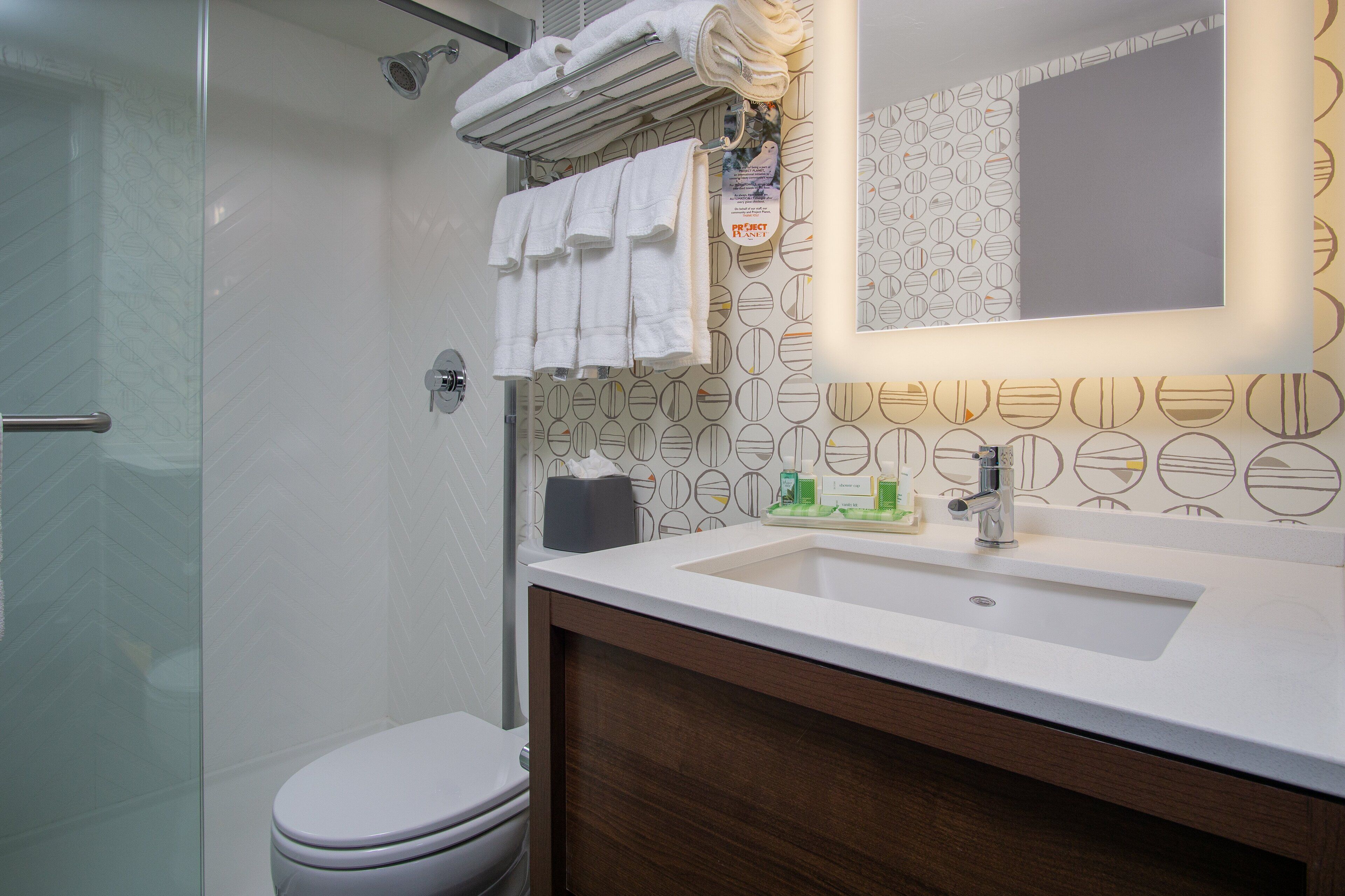 Un bagno moderno con cabina doccia in vetro, un water bianco, un mobile lavabo con specchio e un lavandino con articoli da toilette.