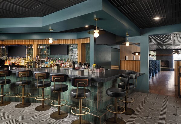 A bar area with multiple stools, a bar counter, and a variety of bottles.