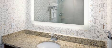 Een badkamer met een granieten aanrechtblad, een wastafel, een spiegel en een douche.