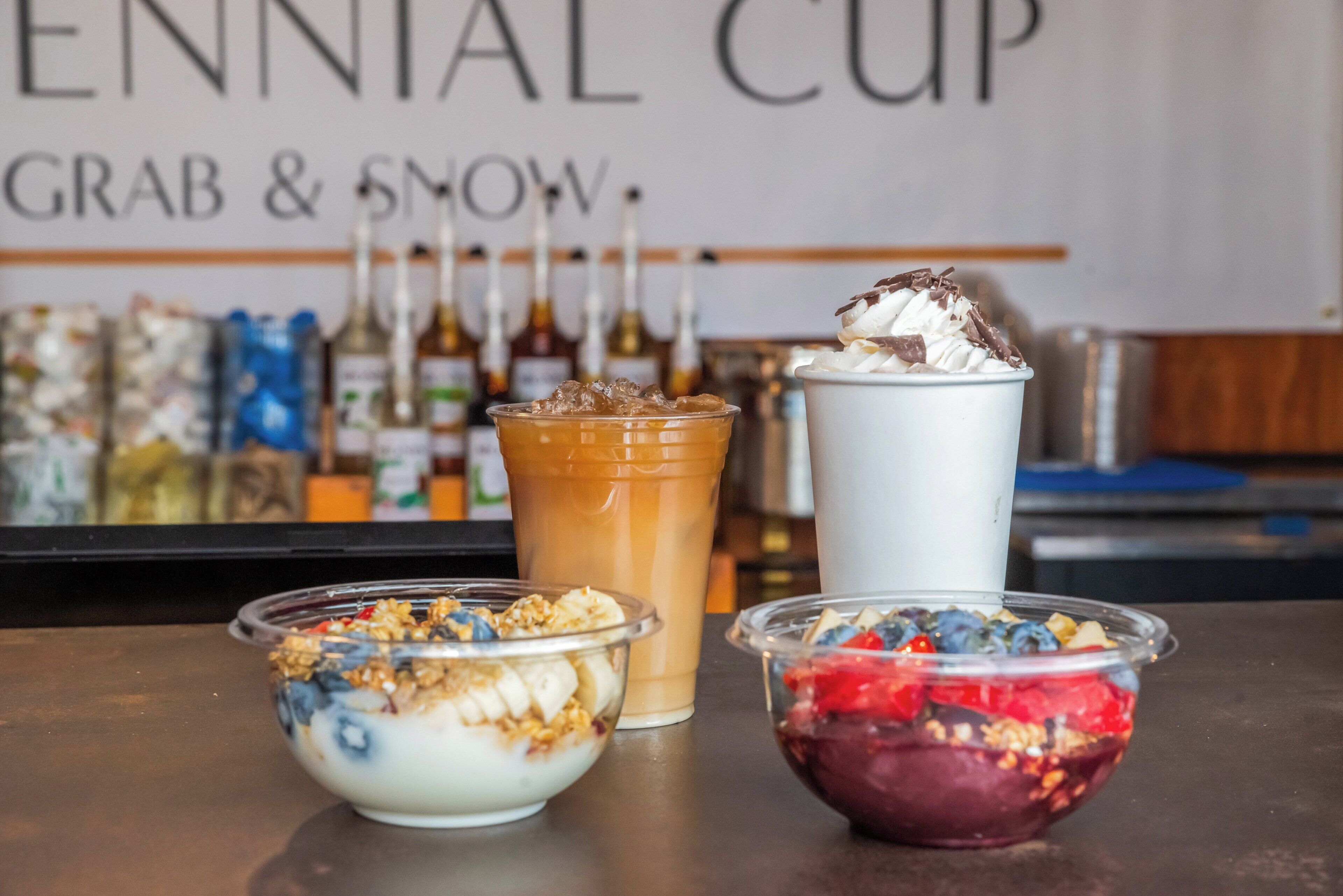 A bar area with three drinks and two bowls of granola with fruits.