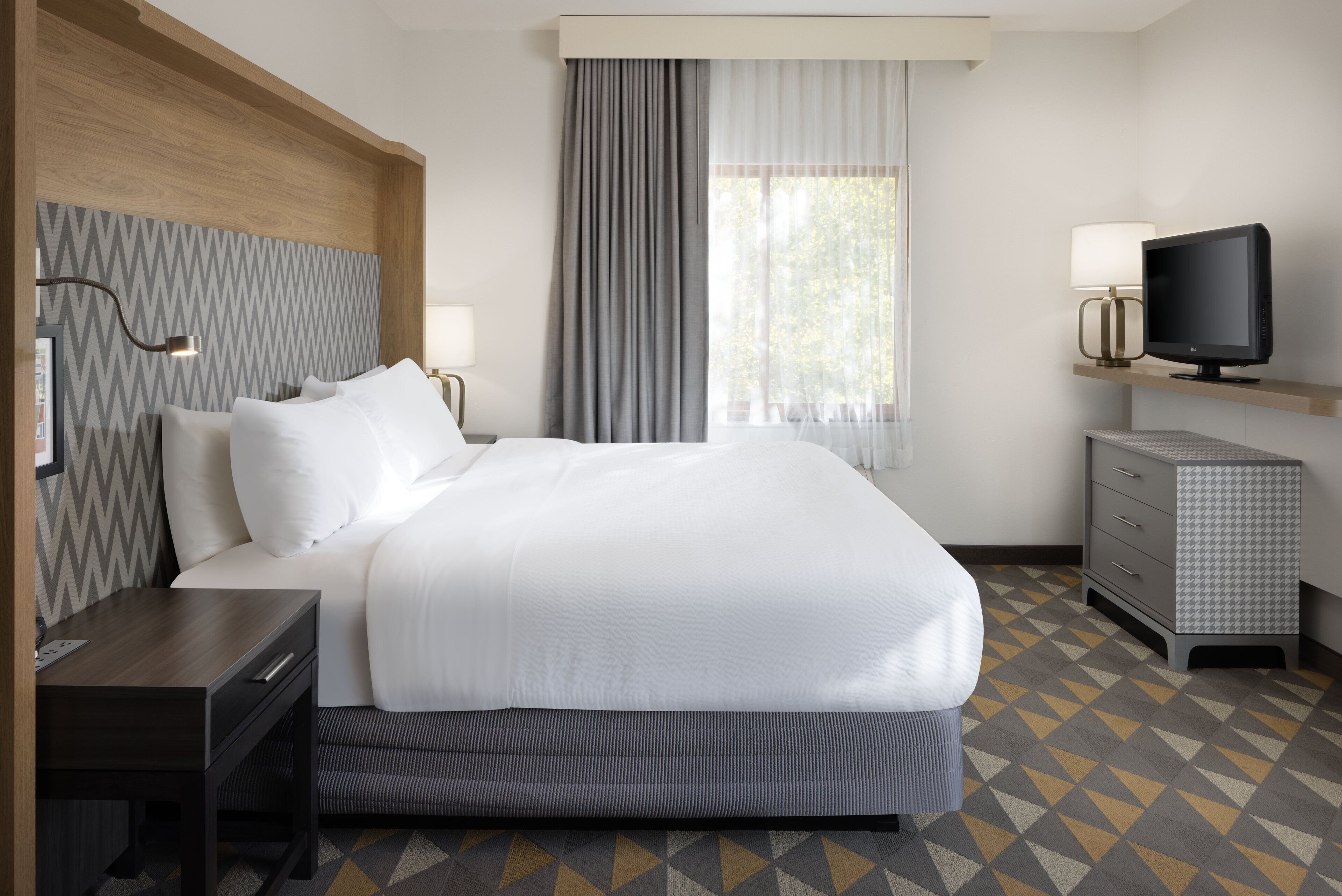 Une chambre d’hôtel avec un grand lit, des tables de chevet, une télévision et une commode.