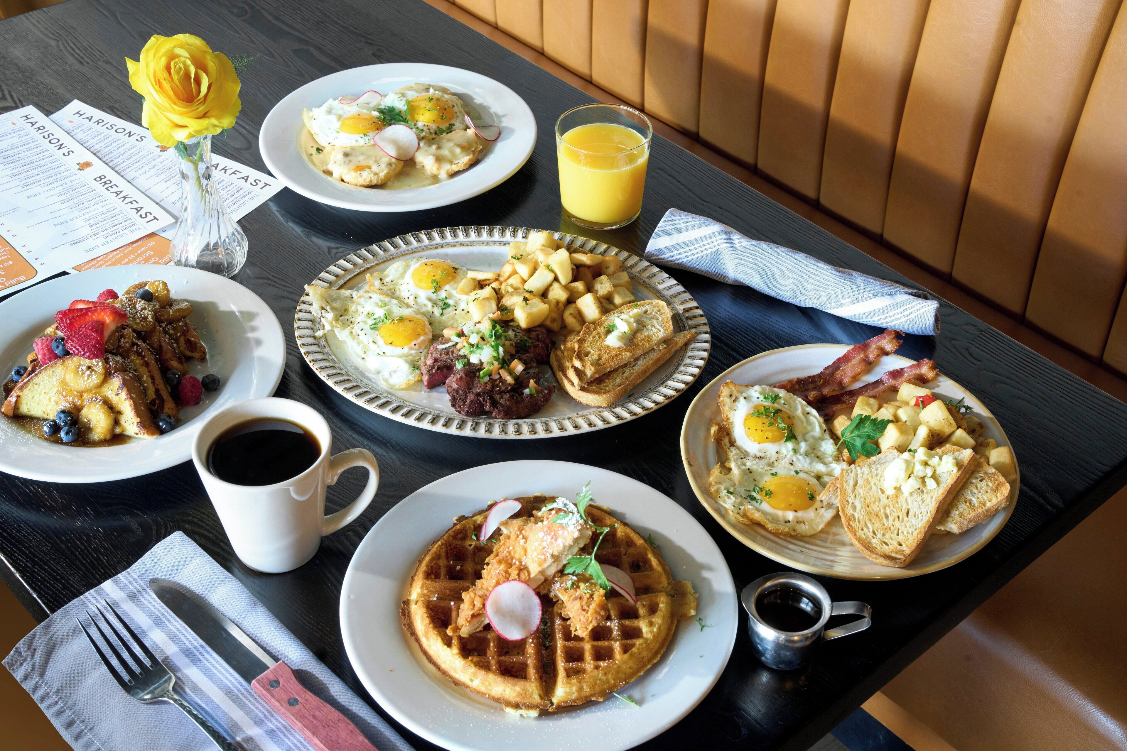 A breakfast table with various dishes including waffles, eggs, and toast, accompanied by a cup of coffee and a glass of orange juice.