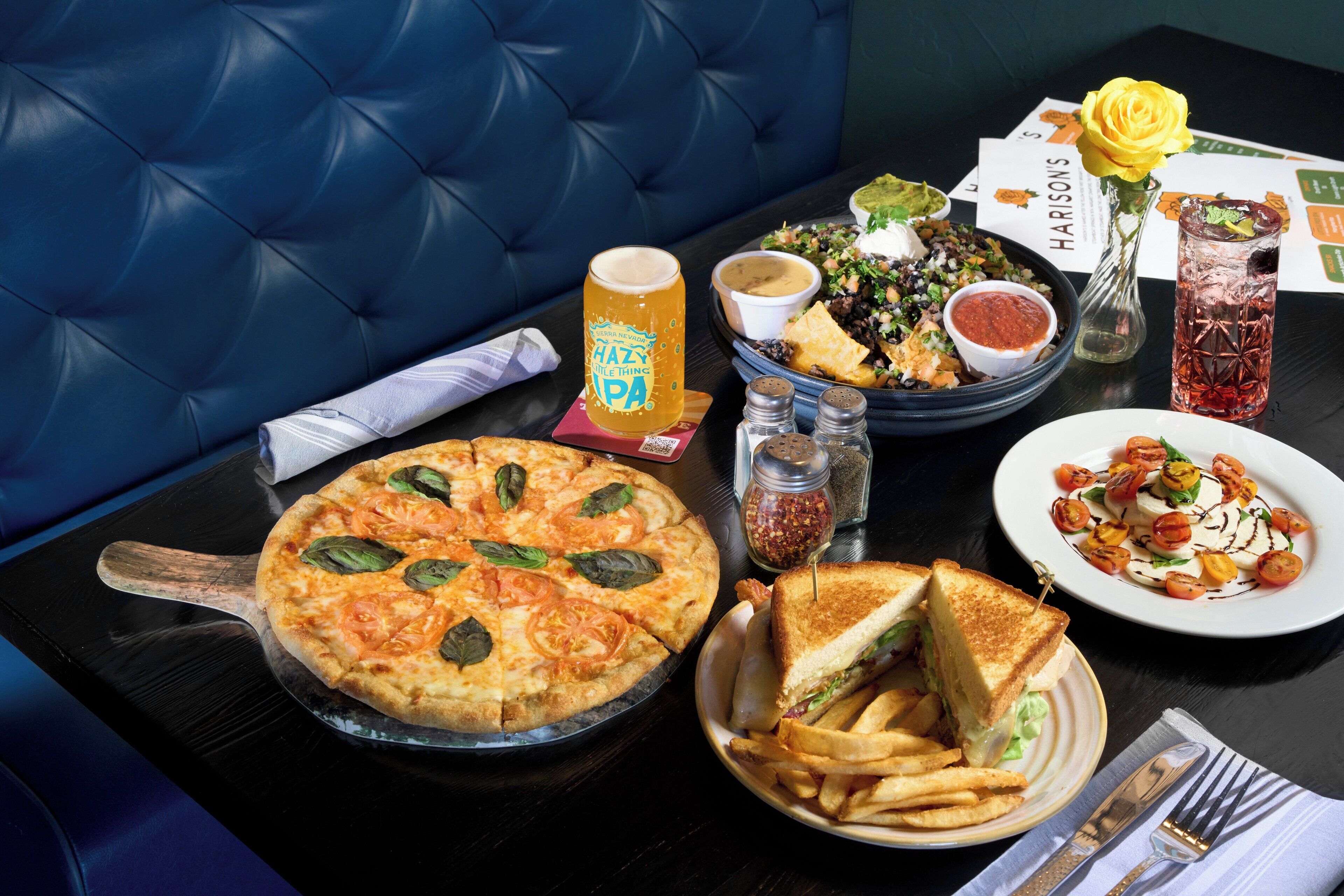 Una mesa de comedor con pizza, sándwich, papas fritas, ensalada y una bebida.