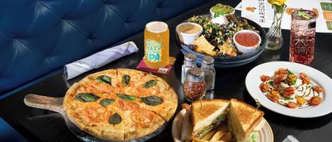 Una mesa de comedor con pizza, sándwich, papas fritas, ensalada y una bebida.