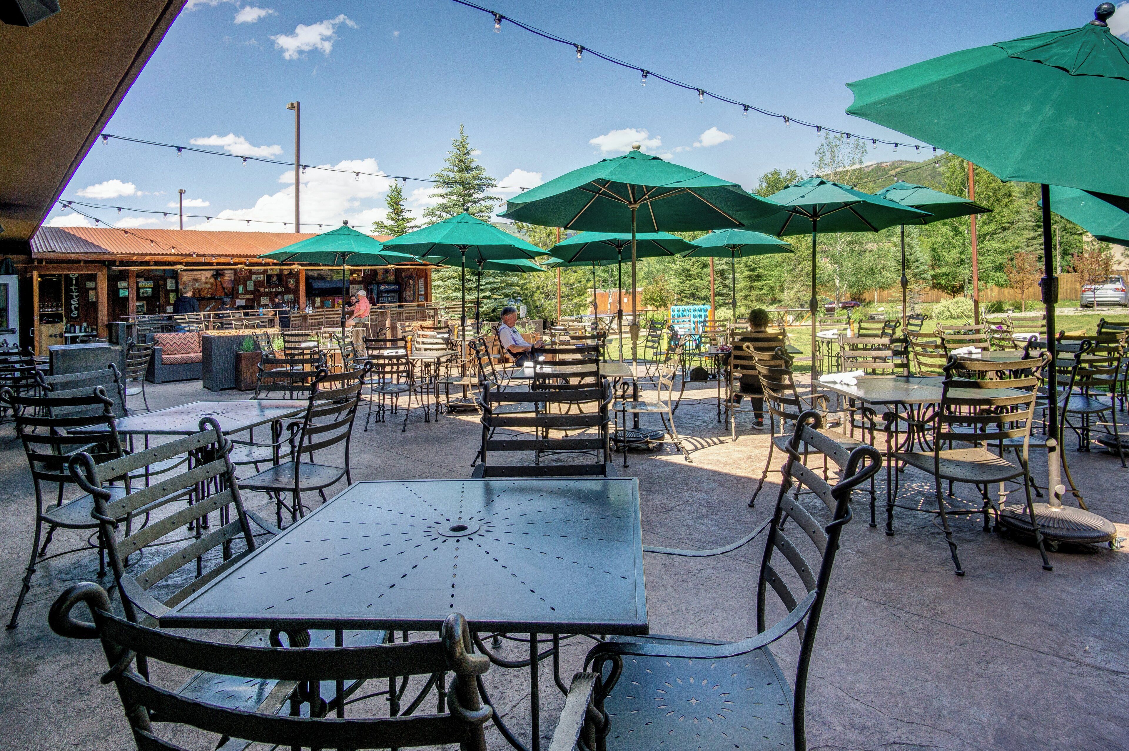 An outdoor patio with tables and chairs, green umbrellas, and a building in the background.