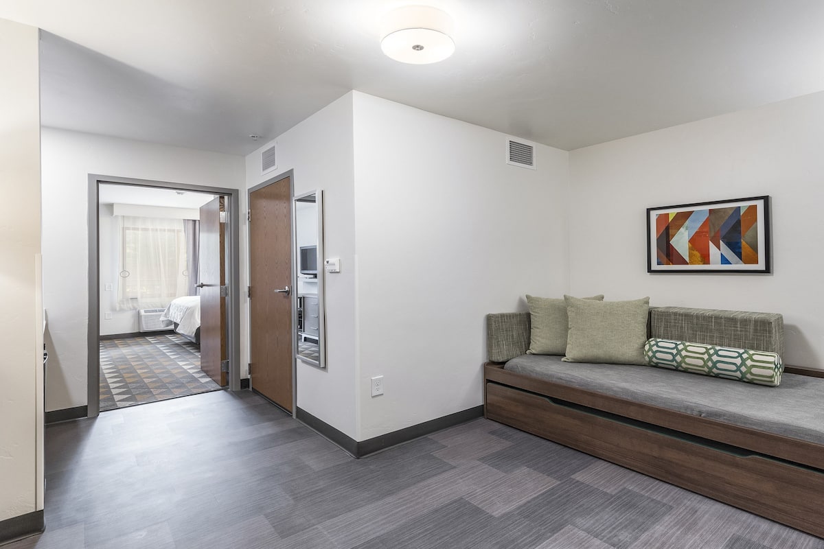 Una habitación de hotel moderna con sofá cama, televisión y un cuadro en la pared.
