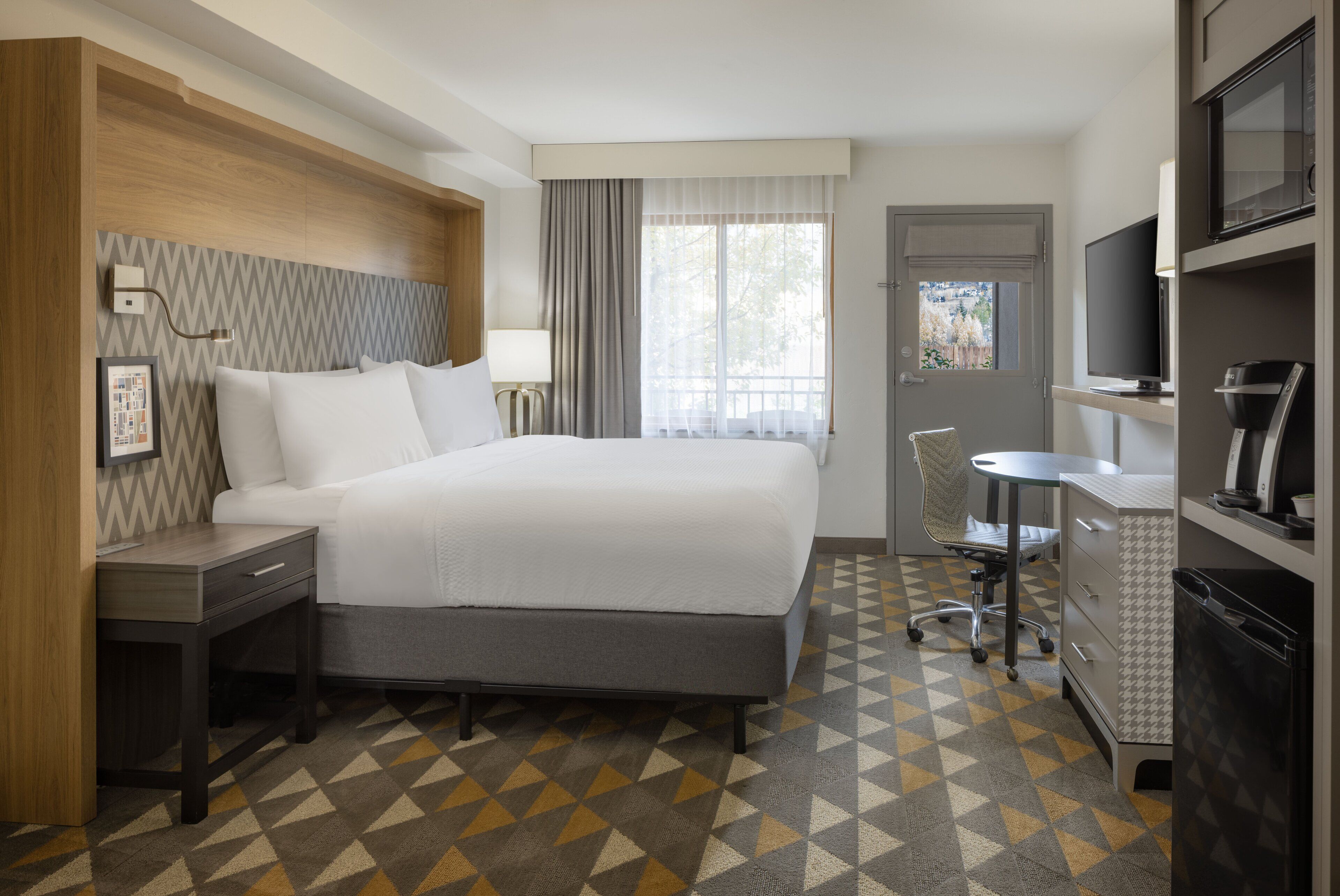 Una habitación de hotel con una cama, un escritorio, una silla, un televisor y un minibar.