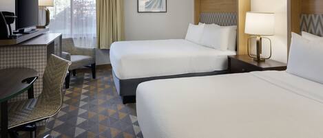 Ein Hotelzimmer mit zwei Betten, einem Schreibtisch mit Fernseher, einem Sessel und einem gestreiften Boden.