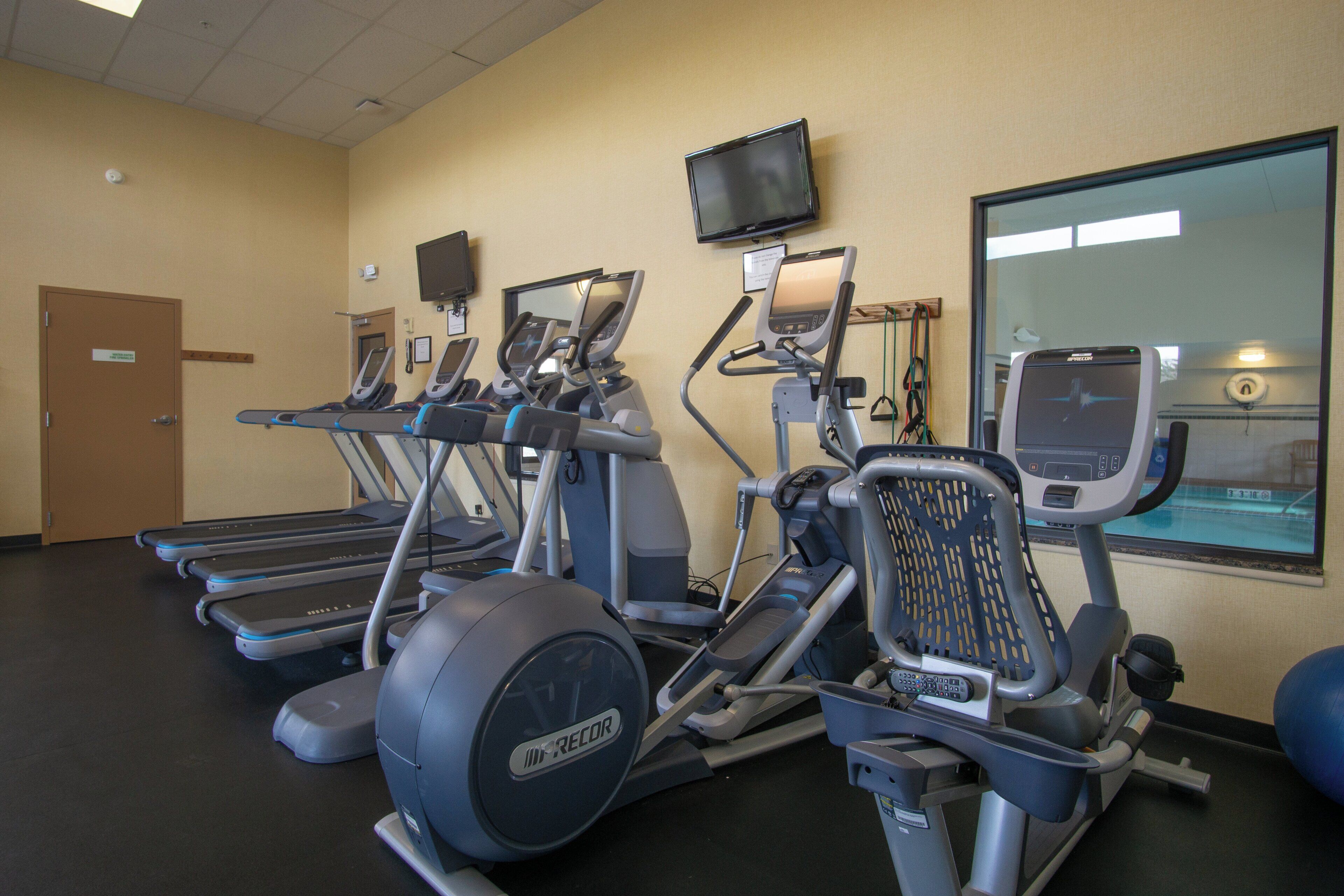 A fitness center with treadmills, elliptical machines, and a TV screen.