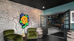 A modern interior with a stone wall, neon art, green chairs, wooden barrels, and a bar area.